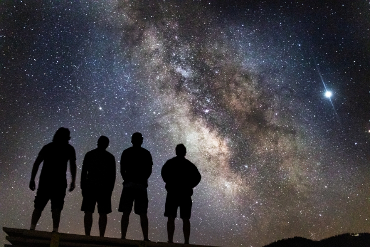 silhouette of four men looking at the sky full of stars