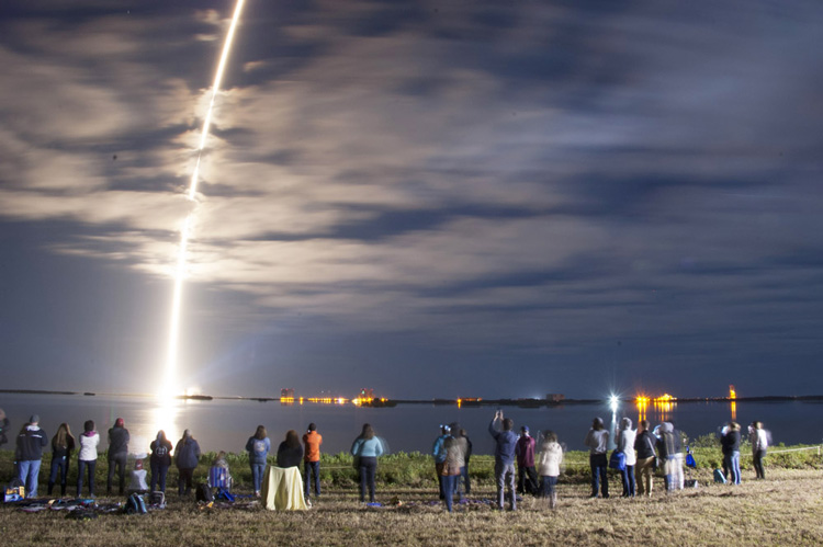 people watching a space rocket launch at night