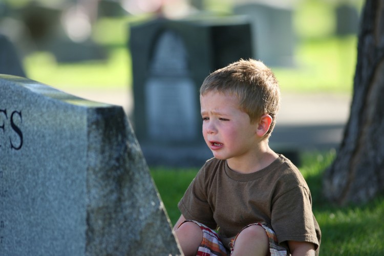 Grieving young boy sitting near a headstone