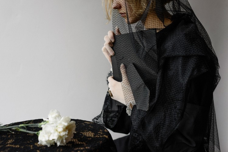 Grieving person with white carnation and funeral veil, holding framed photo at a cremation memorial service