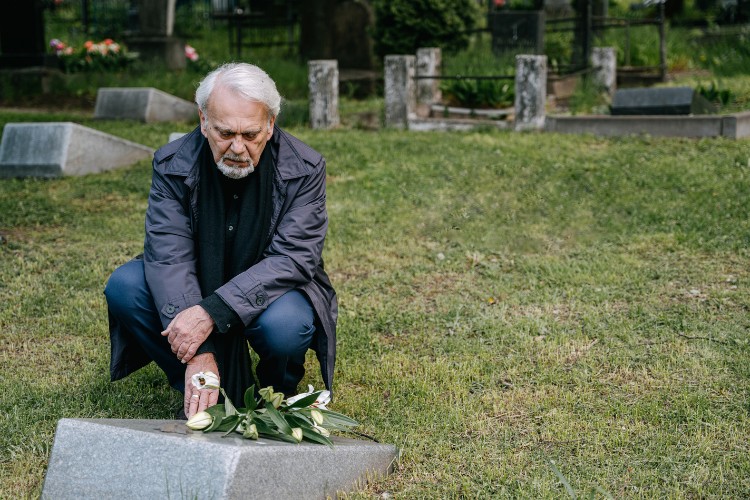 Senior grieving beside a headstone, symbolizing the emotional importance of selecting the right memorial keepsake