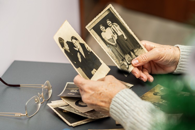 Elderly hands holding vintage photos while choosing meaningful images for a memorial keepsake
